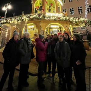 Gruppe älterer Frauen auf einem festlich beleuchteten Weihnachtsmarkt vor einem Glühweinstand