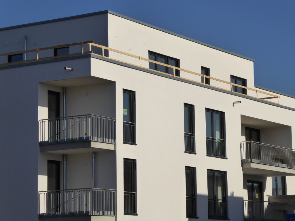 Modernes Wohngebäude mit weißer Fassade, klaren Linien, großen Fenstern und mehreren Balkonen in zeitgemäßer Architektur.