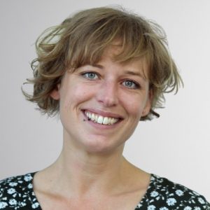 Porträt einer lächelnden Frau mit kurzen hellbraunen Haaren vor neutralem Hintergrund