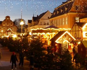 Abendlicher Weihnachtsmarkt mit beleuchteten Holzständen, Tannenbäumen und festlicher Straßenbeleuchtung.